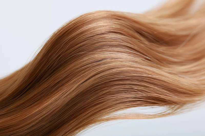 Flowing wave of straight golden-brown hair suspended midair against white background