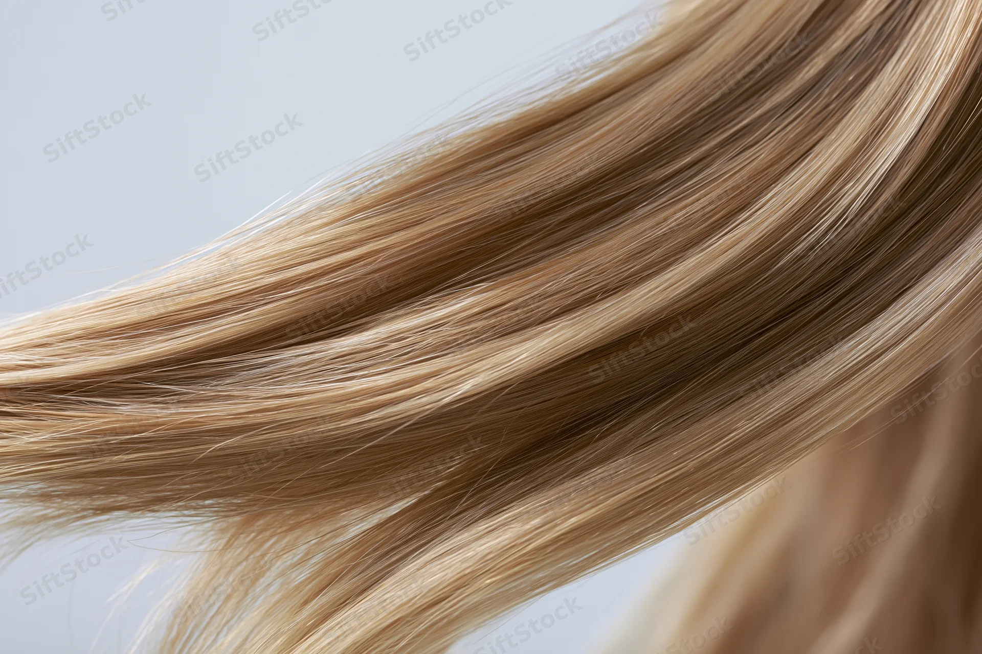 Flowing straight blonde hair strands in closeup against light background