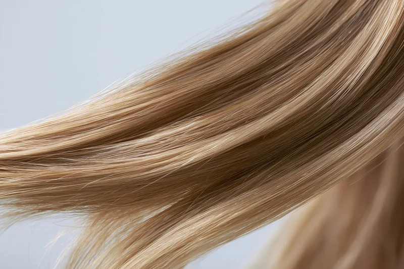 Flowing straight blonde hair strands in closeup against light background