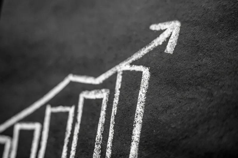Upward arrow and bar chart drawn in chalk on a blackboard surface