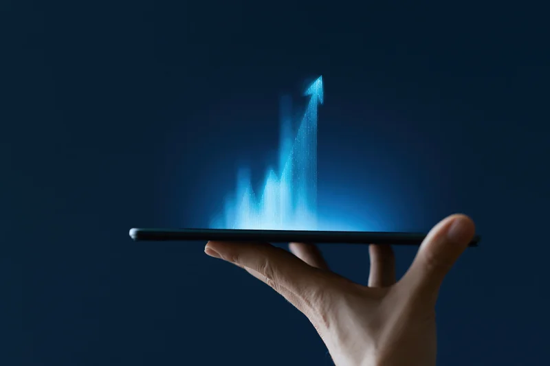 Hand holding tablet with glowing blue holographic graph rising upward against dark background