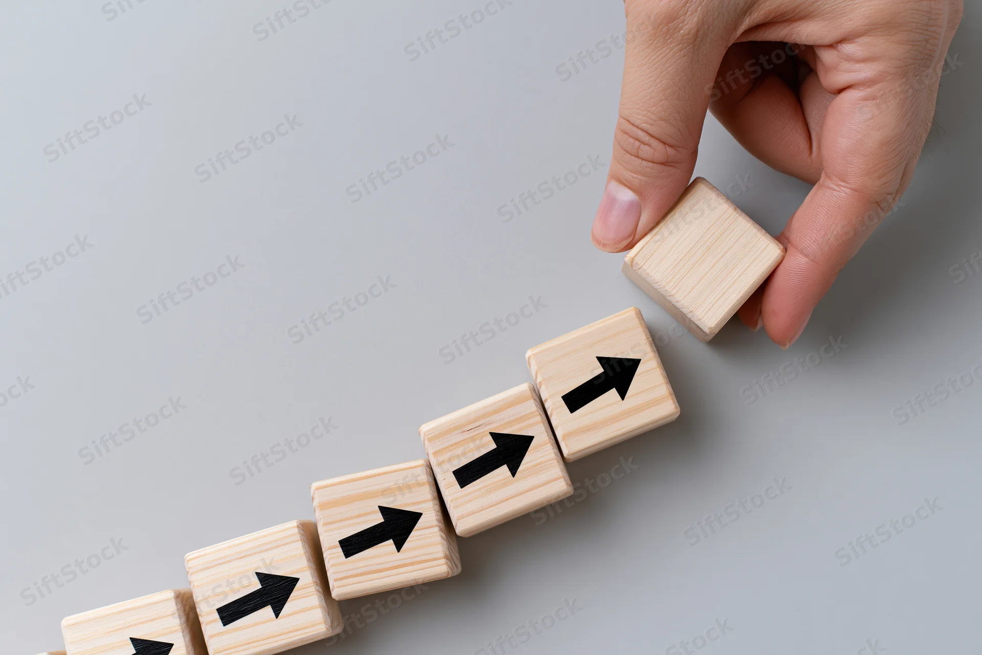 Hand placing wooden cube with arrow on staircase of similar cubes on gray surface