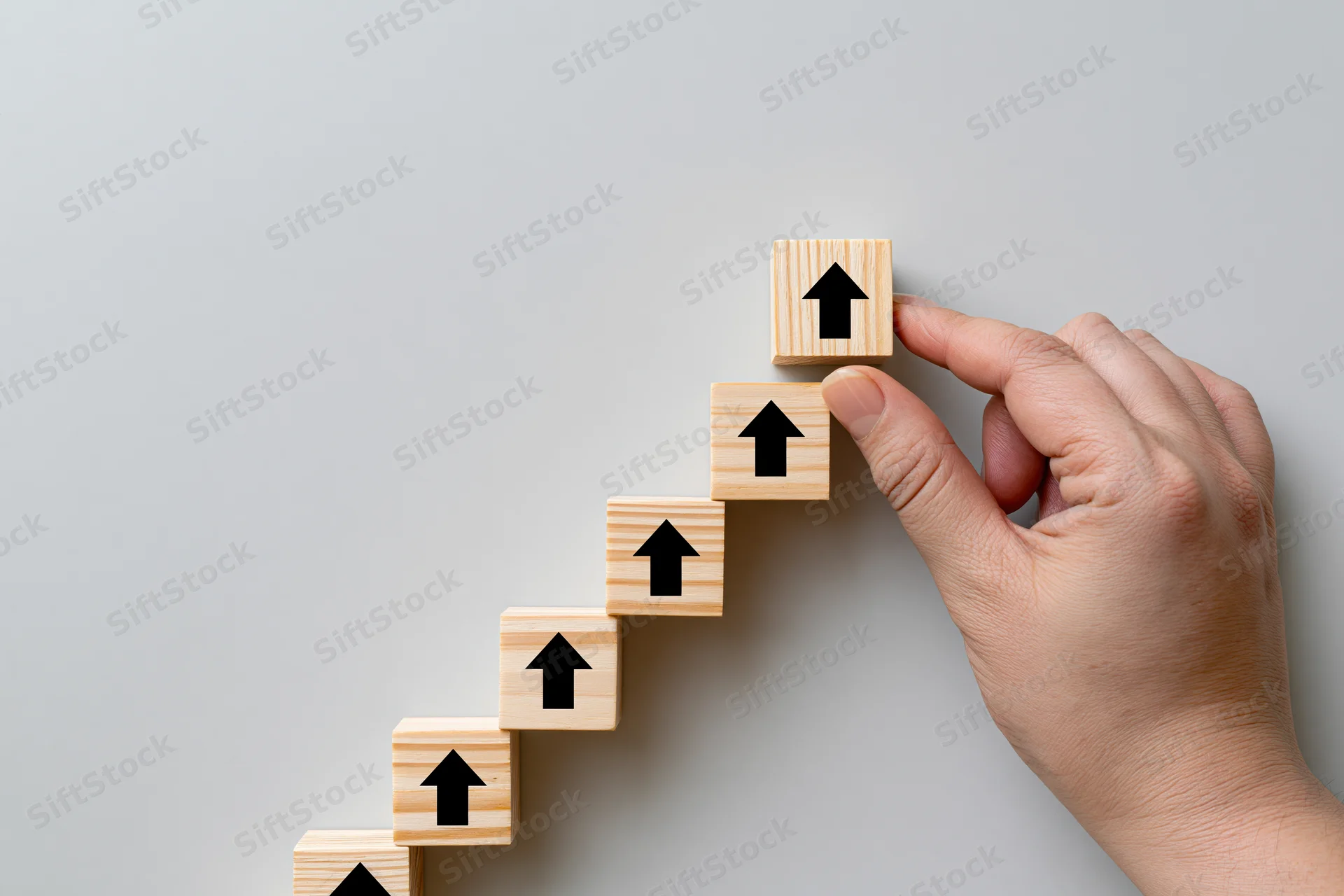 Hand placing final wooden cube with upward arrow on staircase against gray background