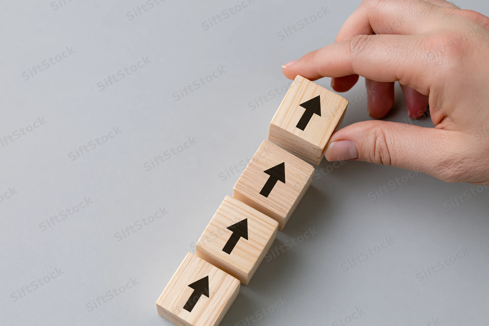 Hand placing wooden cube with arrow on staircase of cubes on gray surface