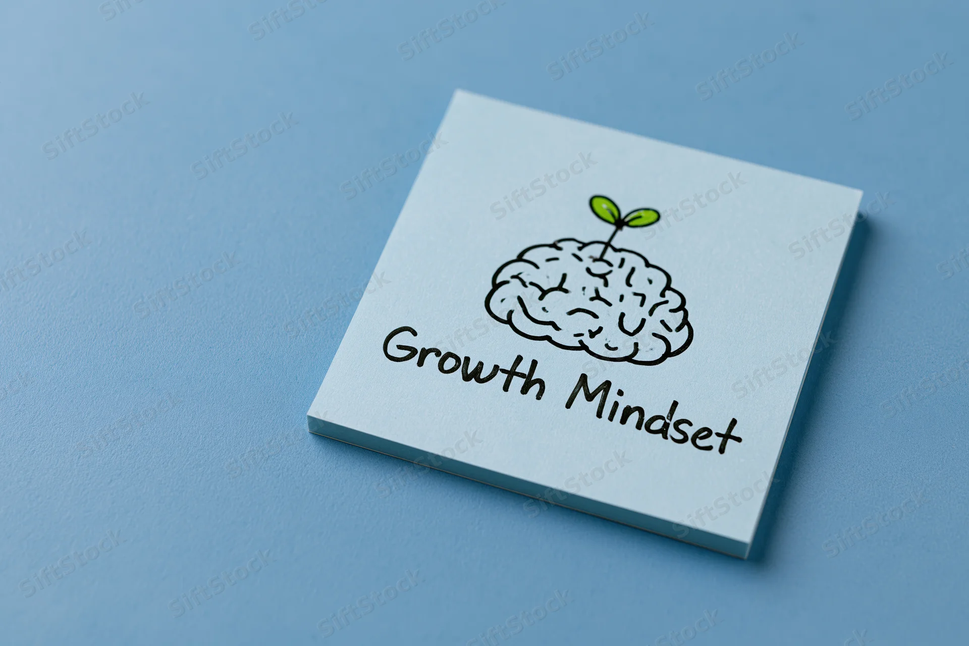 Light blue sticky note with hand-drawn brain and sprout illustration labeled growth mindset on blue surface