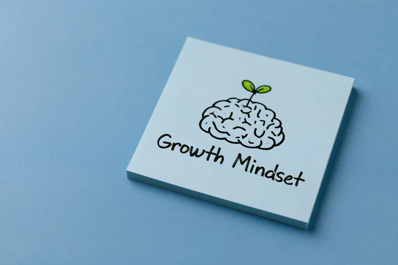 Light blue sticky note with hand-drawn brain and sprout illustration labeled growth mindset on blue surface