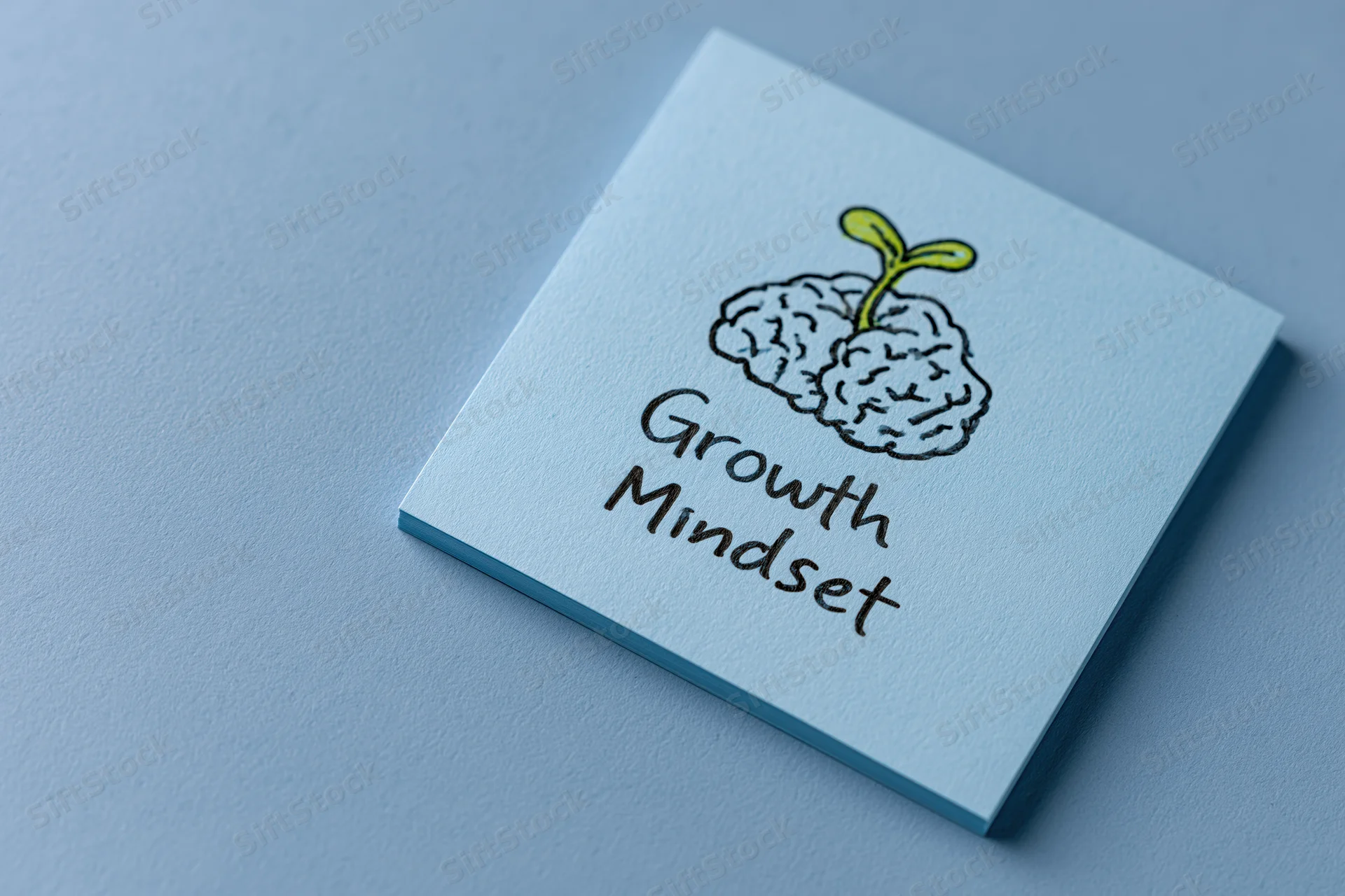 Light blue sticky note with hand-drawn brain and seedling labeled growth mindset on flat blue surface