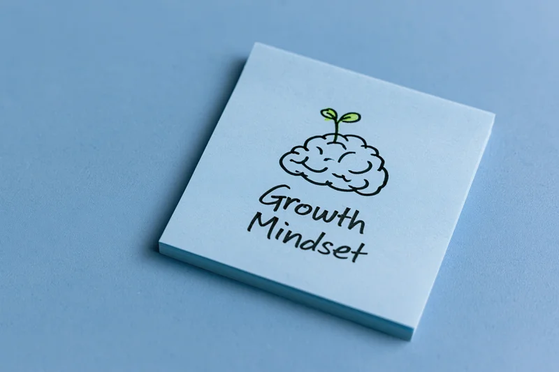 Light blue sticky note with hand-drawn brain and sprout illustration and text growth mindset on flat blue surface