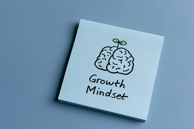 Light blue sticky note with hand-drawn brain and sprout illustration and text growth mindset on flat blue surface