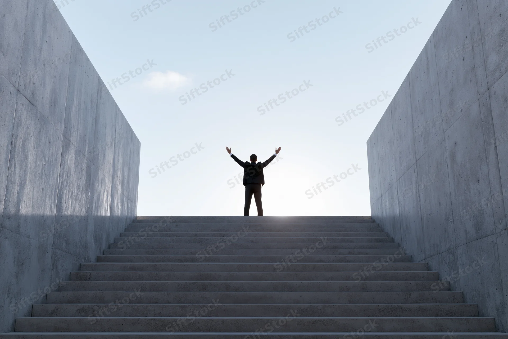 Man in silhouette with arms raised at top of concrete staircase under bright sky