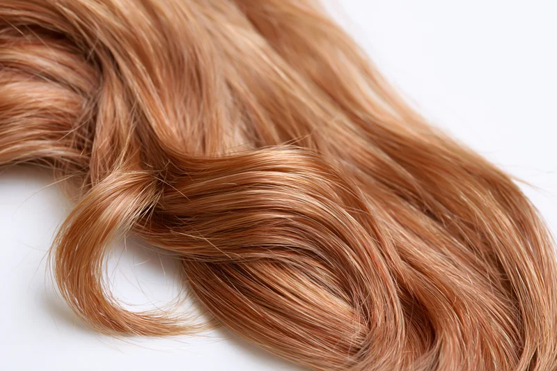 Loose curl of auburn-strawberry blonde human hair lying on white surface