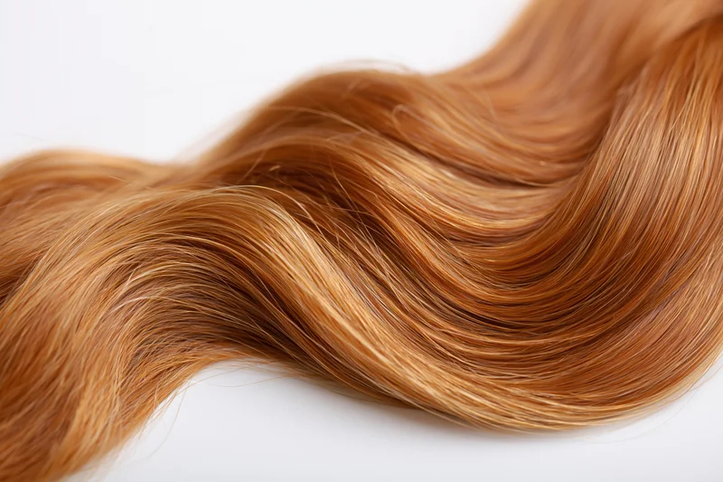Auburn-strawberry blonde human hair curl lying on white surface