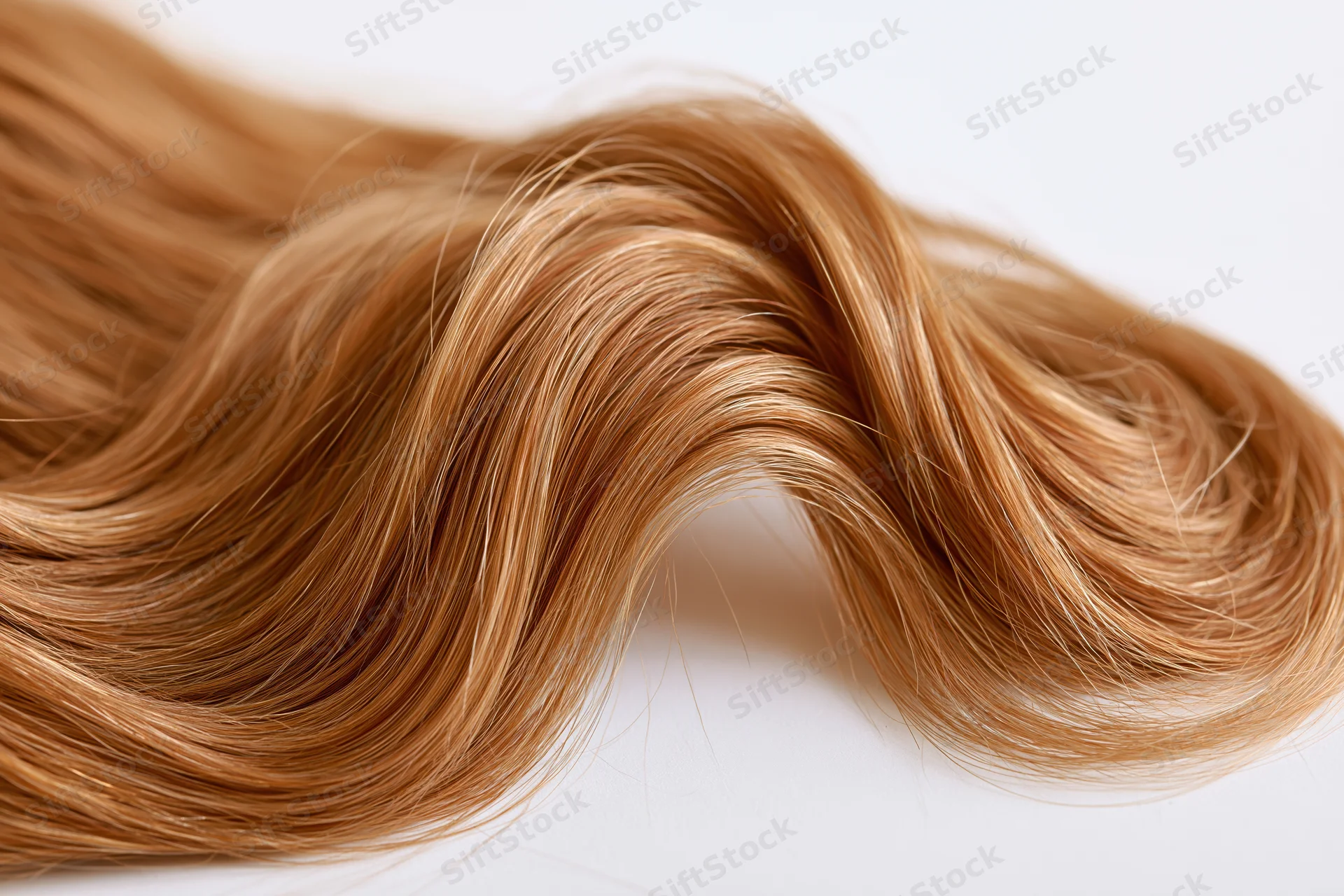 Loose curl of auburn-strawberry blonde human hair lying on white surface