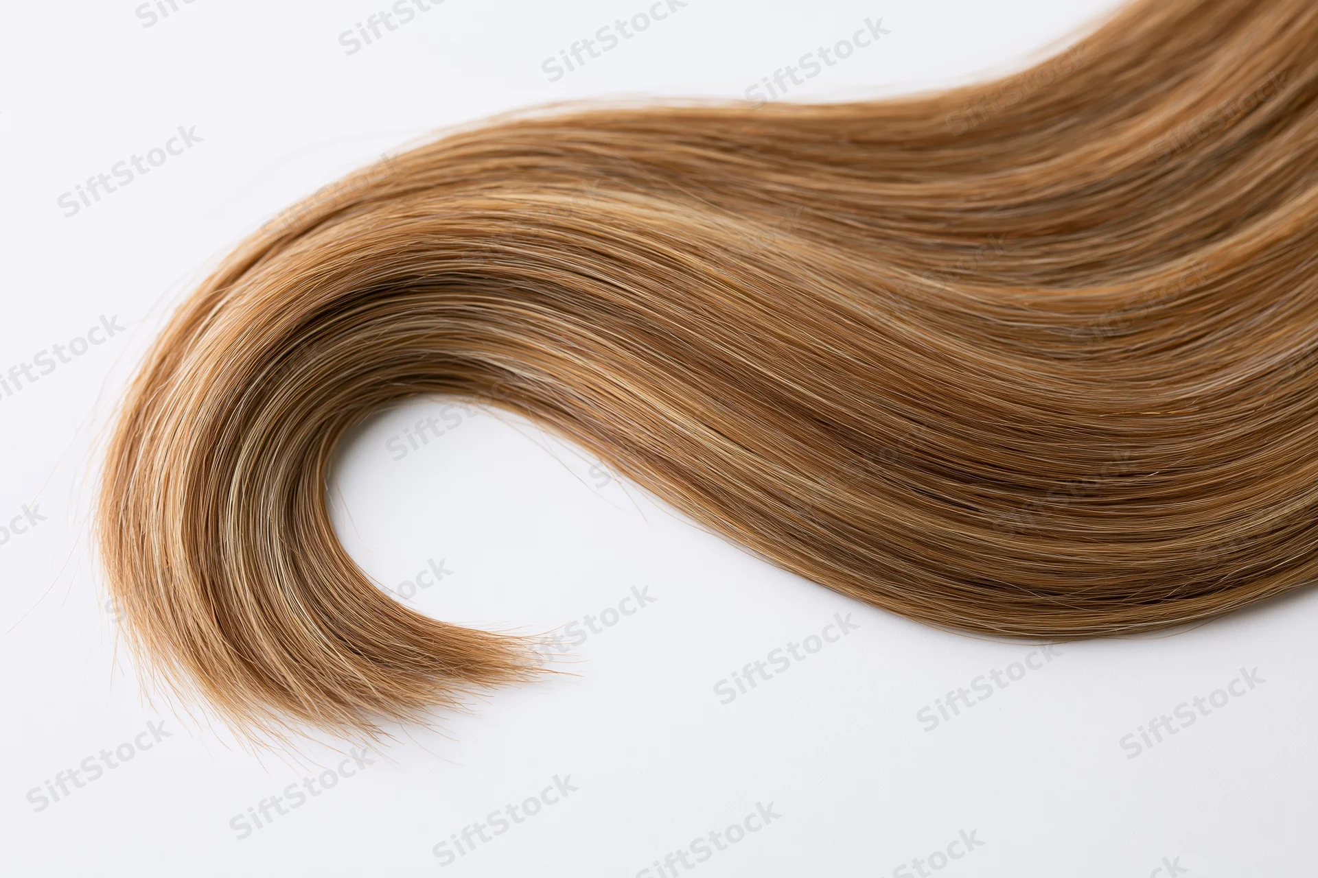 A loose curl of human hair extension laid flat on a white surface