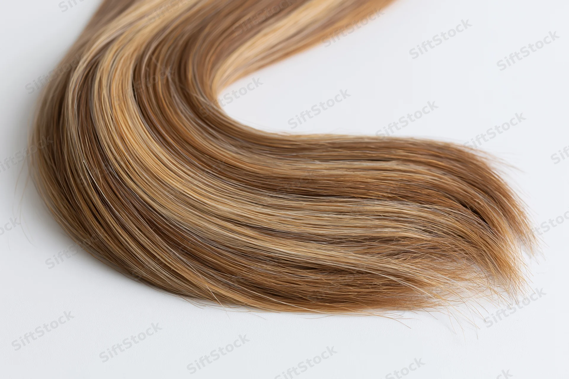 A loose curl of human hair extension laid flat on a white surface