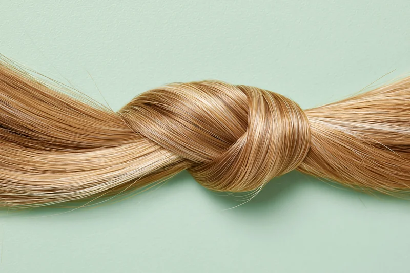 Thick blonde hair strand tied in a loose knot on a flat surface