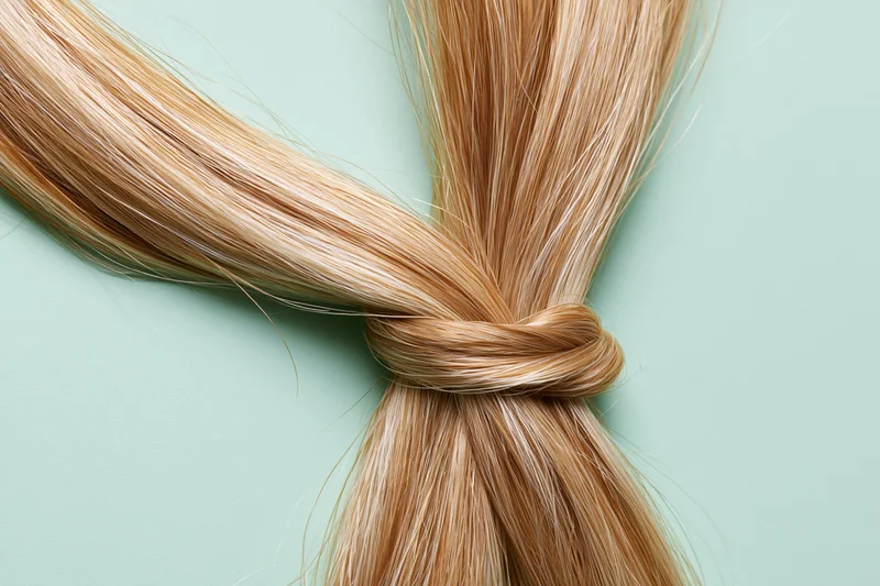Thick blonde hair strand tied in a loose knot laid flat on a light green surface