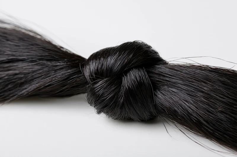 Thick black hair strand tied in a loose overhand knot on white background