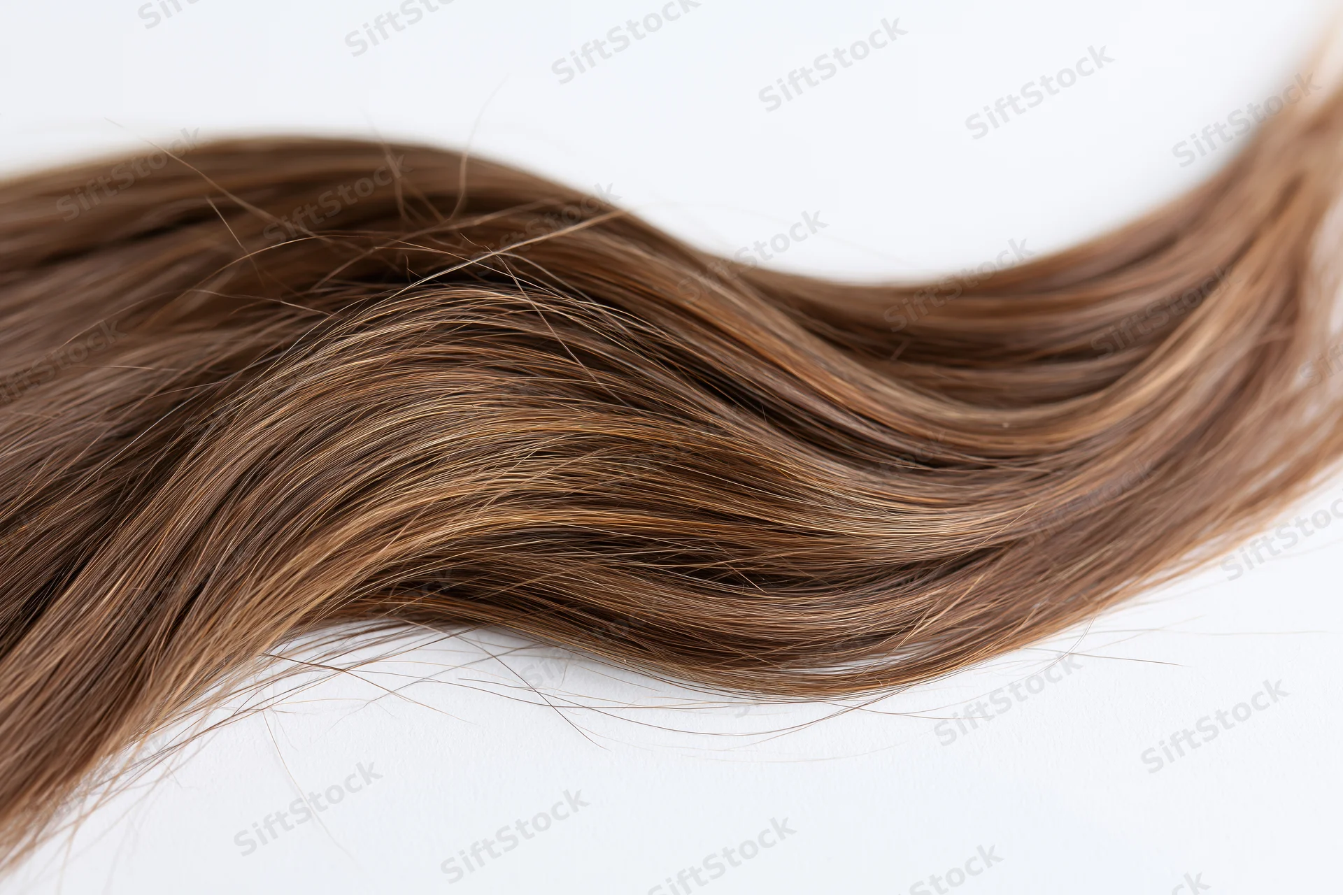 A loose strand of long brown hair with subtle natural highlights lying on a white surface
