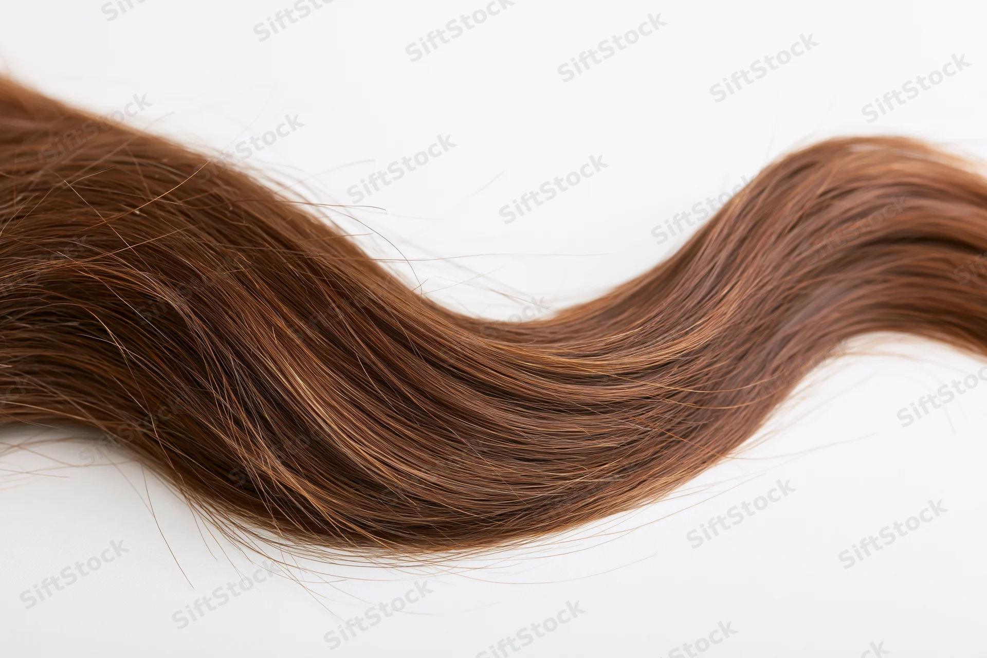 A loose strand of long brown wavy hair with natural highlights on a white background
