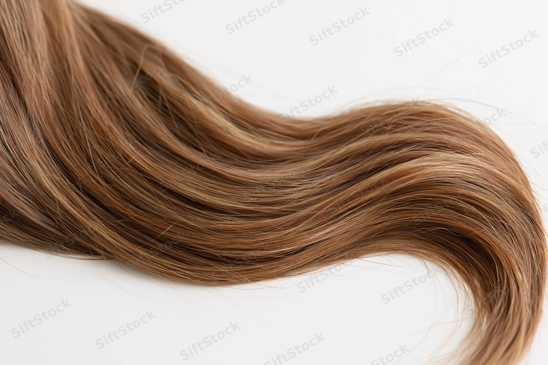 A loose strand of long brown hair with subtle natural highlights flowing across a white surface
