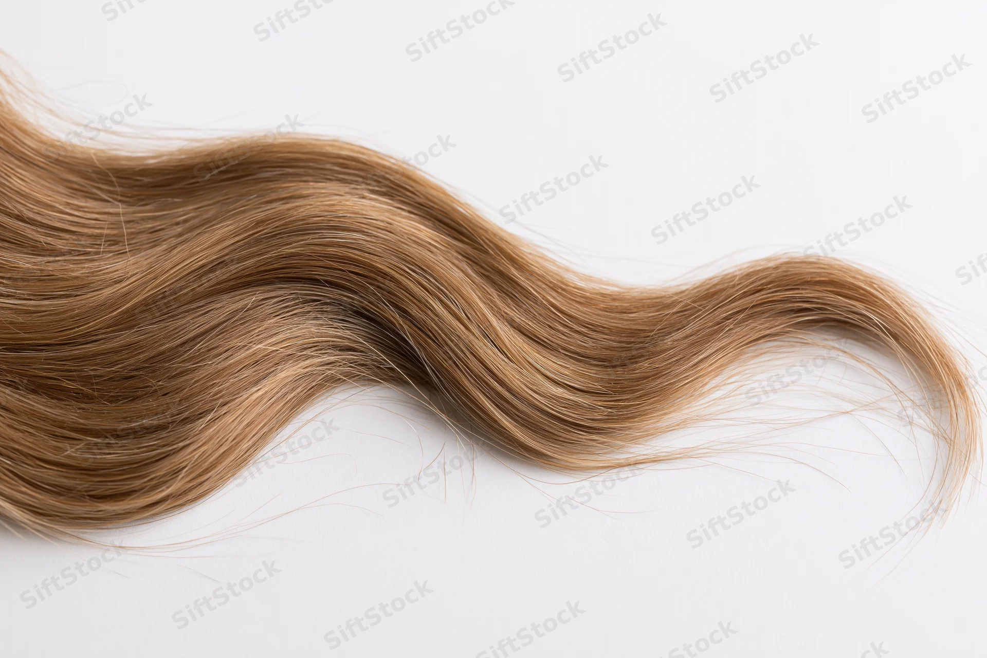 Loose wavy light brown human hair strand lying on white surface