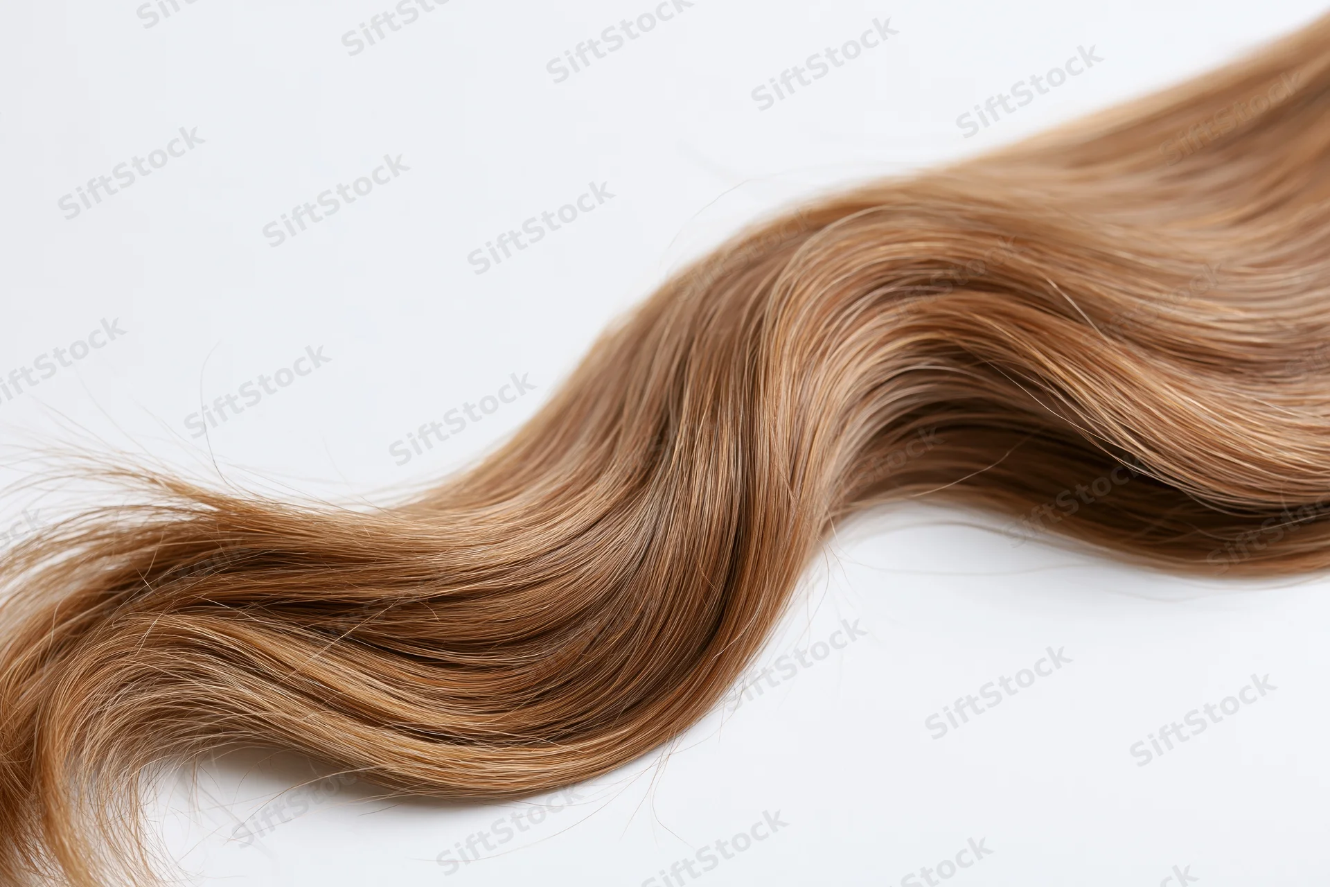 Loose wavy light brown human hair strand lying on white background