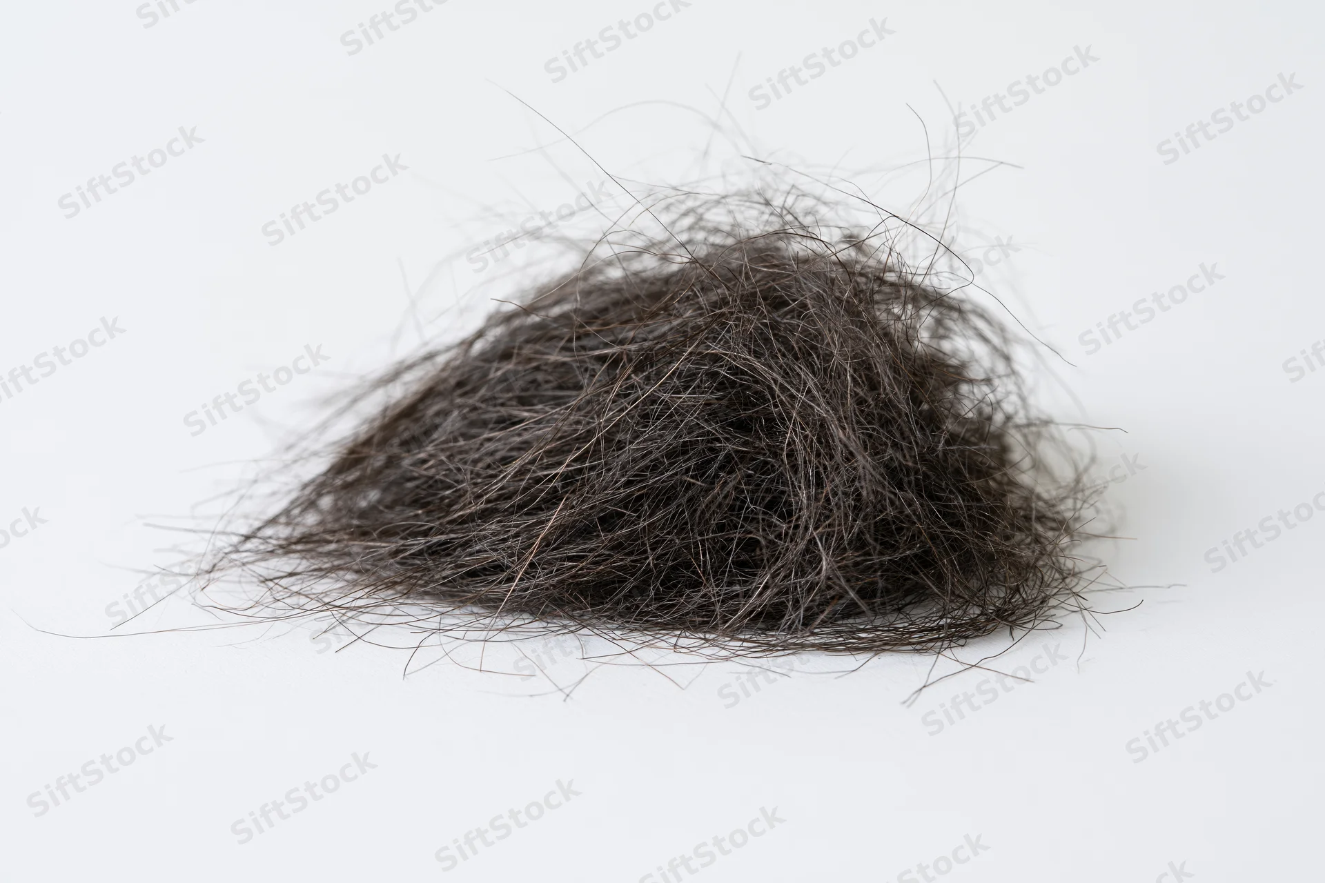 A tangled clump of shed dark human hair resting on a white surface