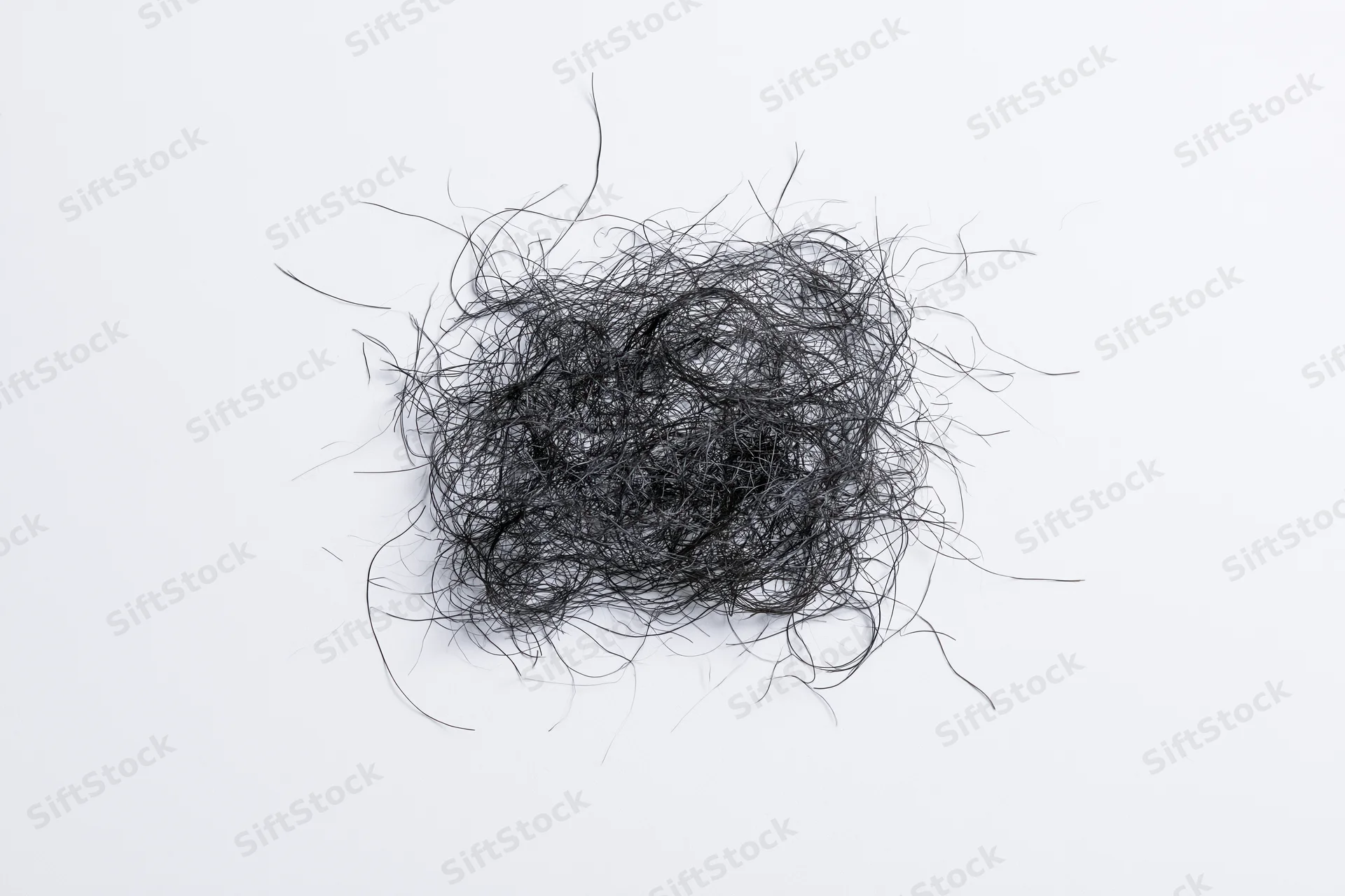 Tangled mass of fine dark hair strands scattered on white surface