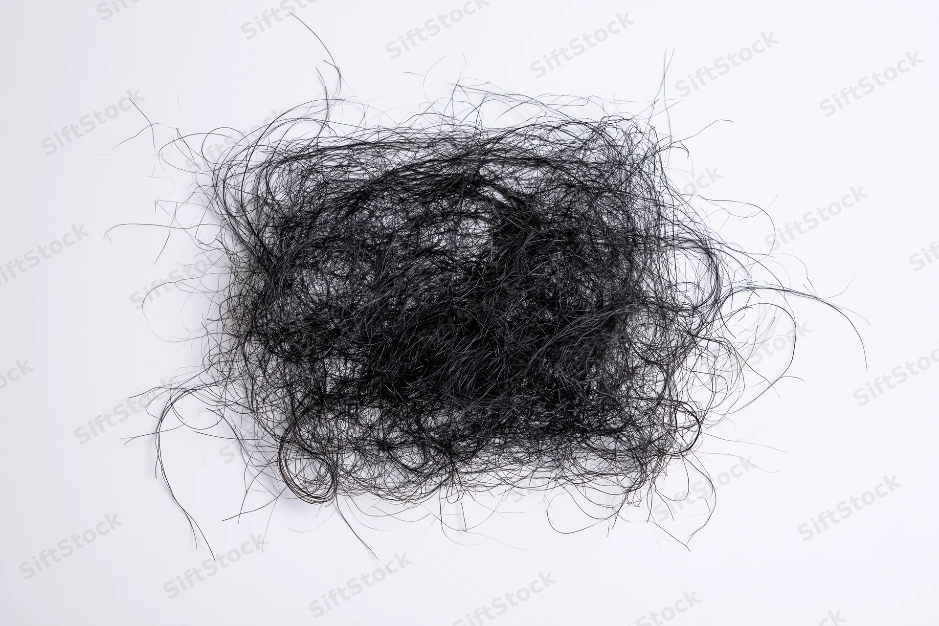 Tangled mass of fine dark hair strands scattered on white surface