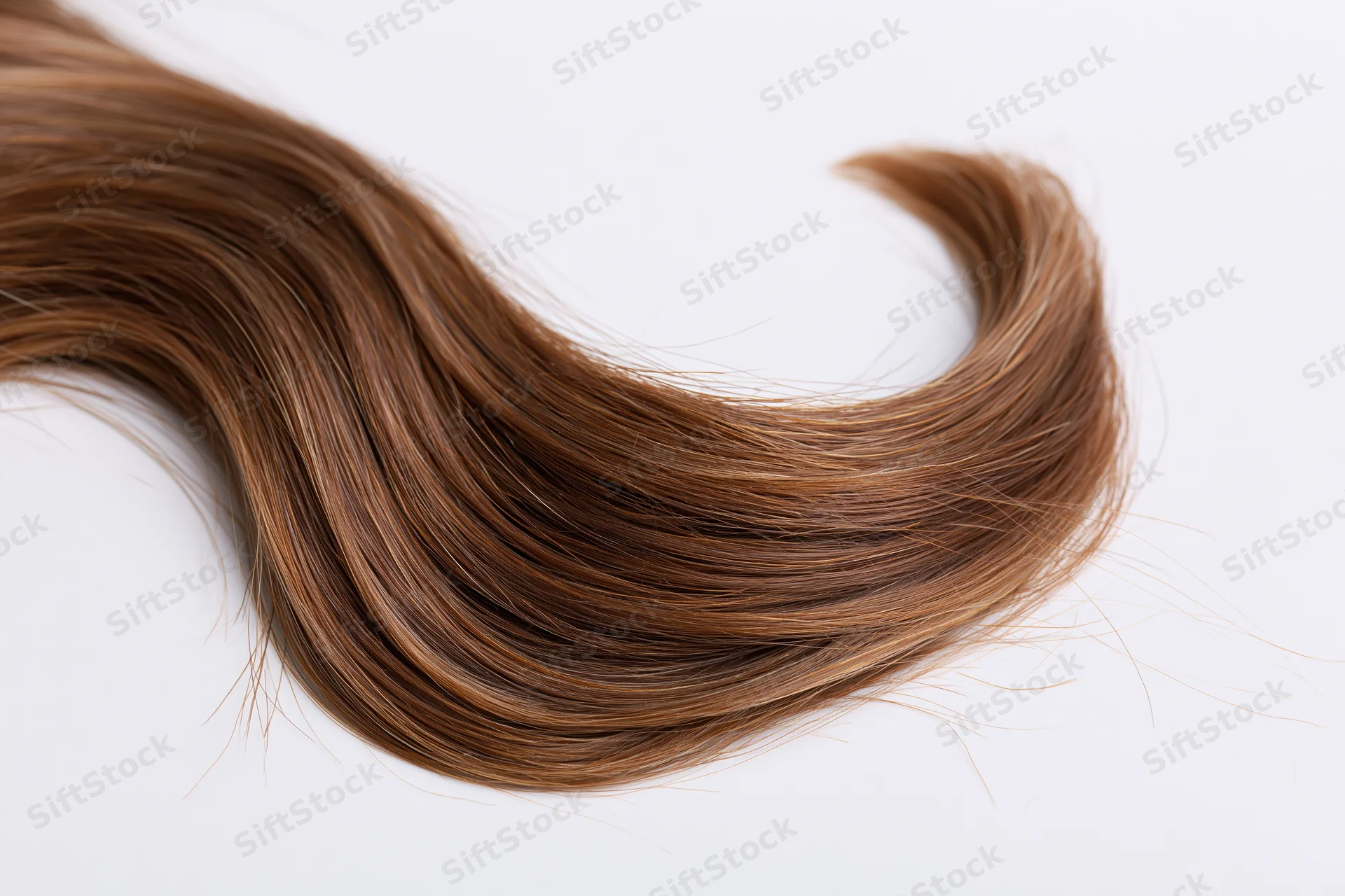 Loose wavy strand of medium brown hair with warm auburn highlights on white background