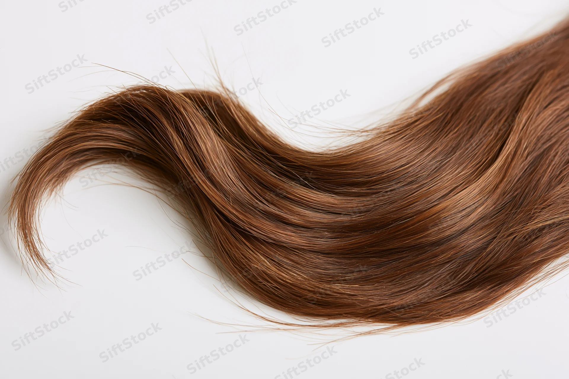 Loose wavy strand of medium brown hair with warm auburn highlights on white background