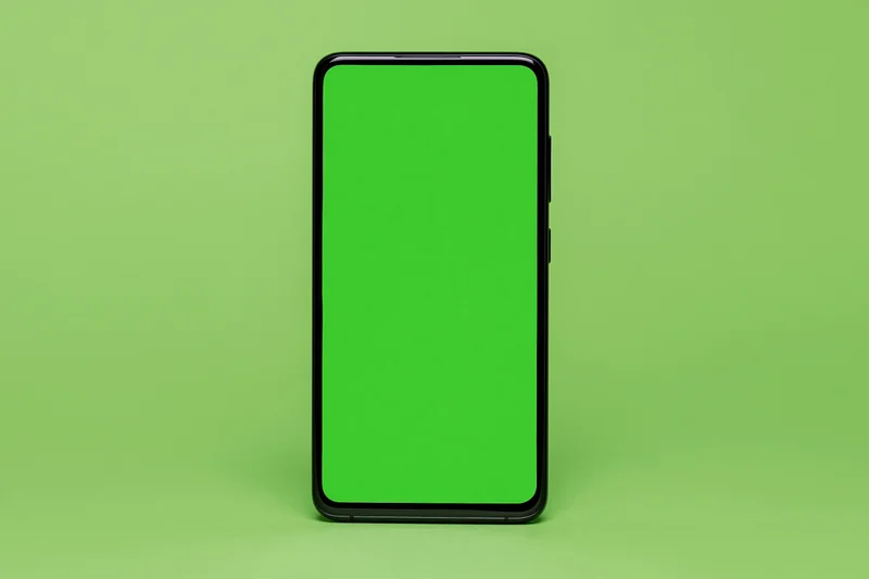 Black-framed smartphone with green screen standing on green surface