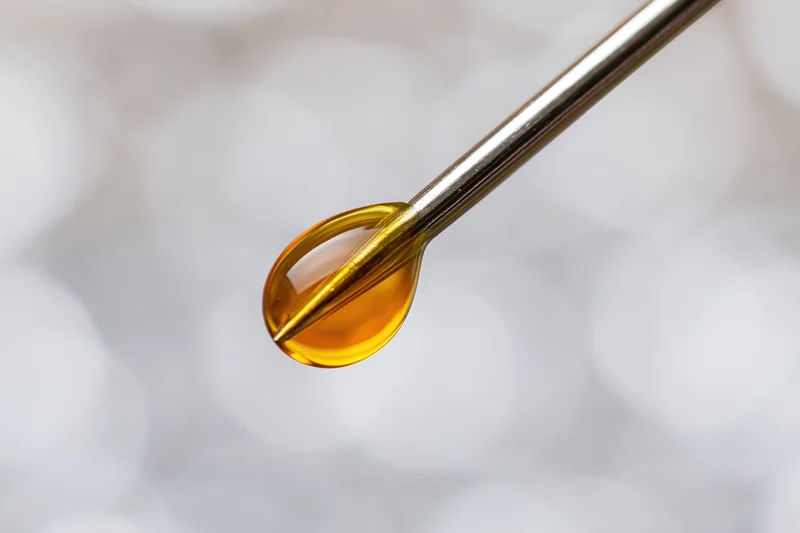 Golden oil droplet suspended on a syringe needle tip in close-up view