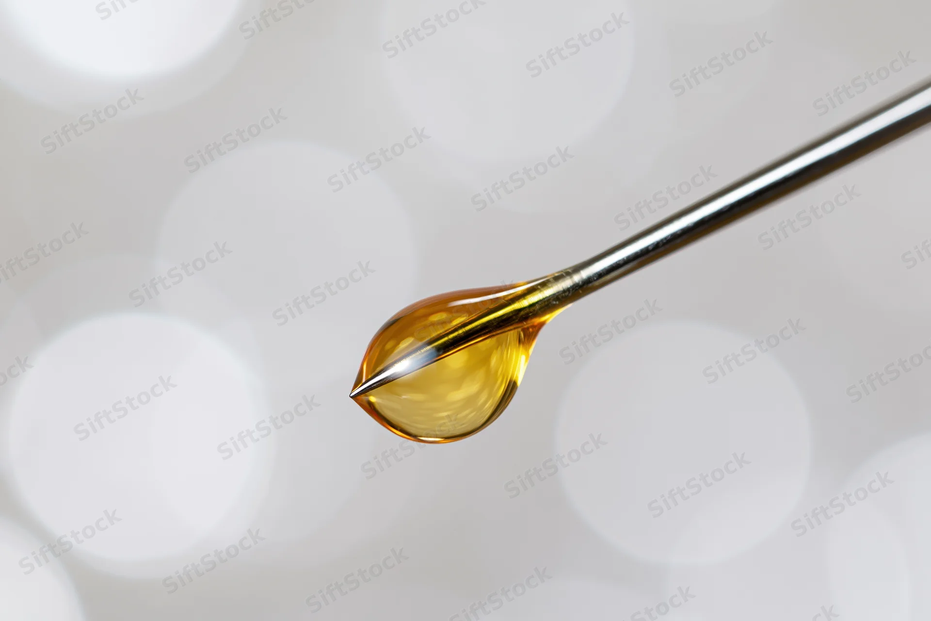 Golden oil droplet suspended on a syringe needle tip against a soft bokeh background