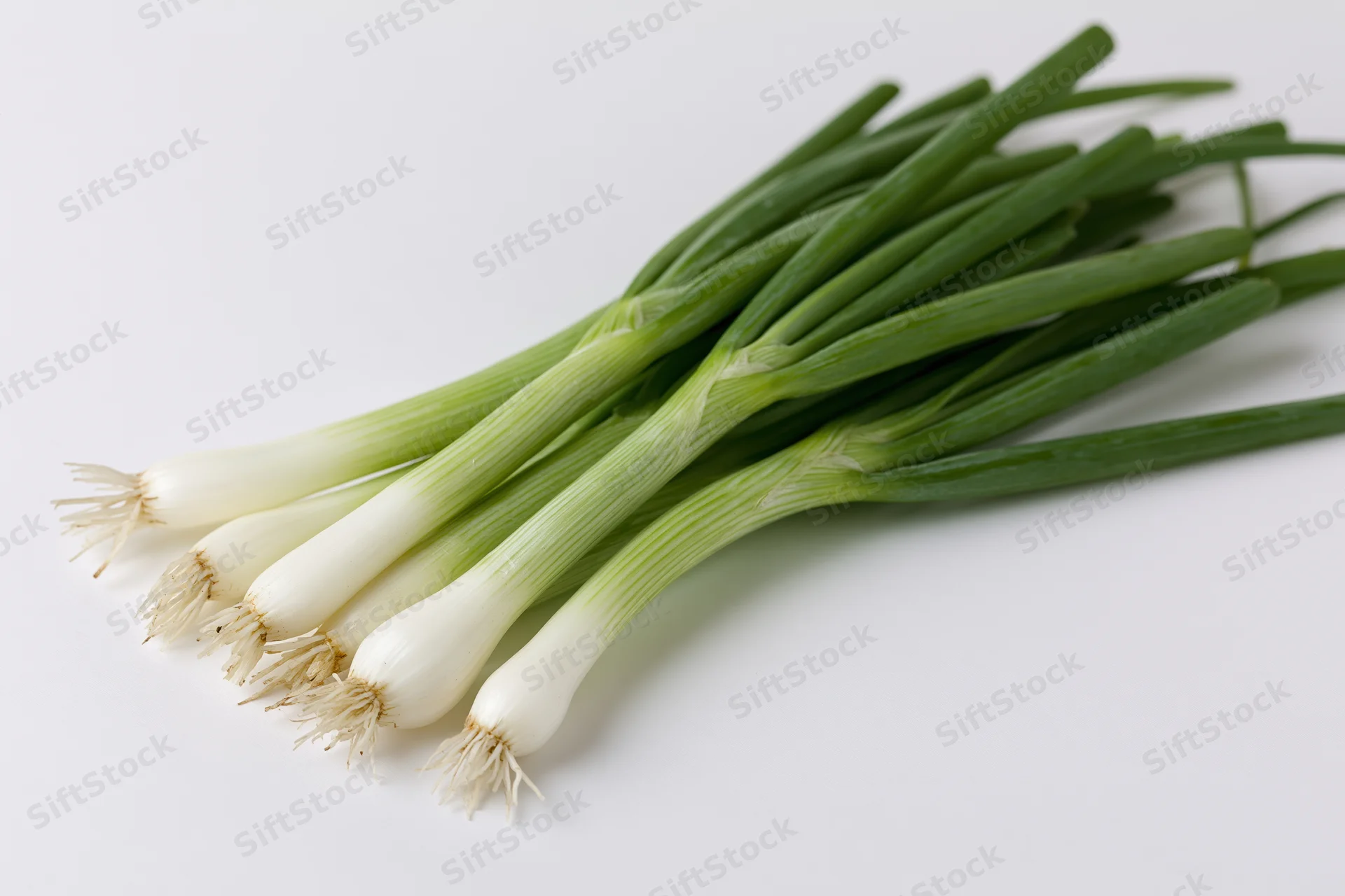 A small bunch of fresh green onions with white bulb ends and green stalks on a white surface