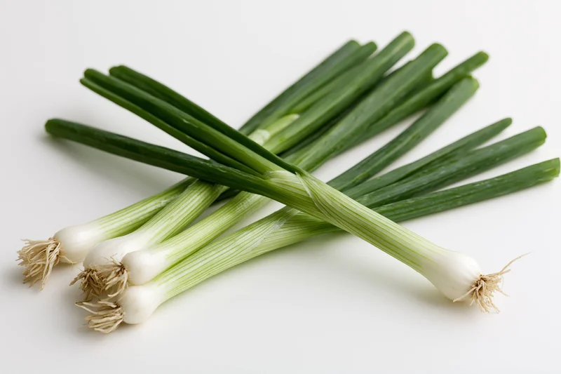 Fresh green onions with white bulbs and green stems arranged on a white surface