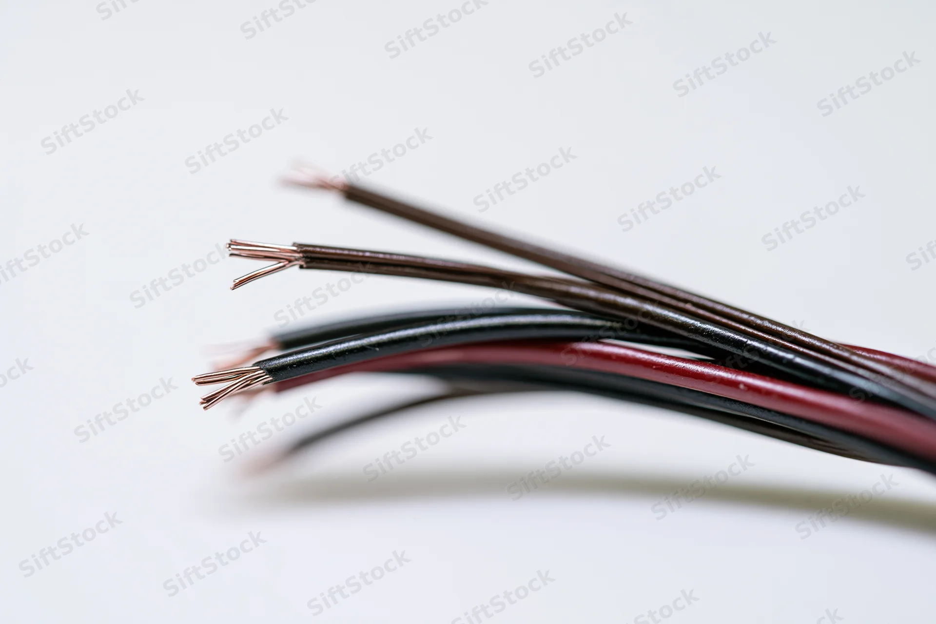 Closeup of thin electrical wires with exposed copper strands fanning apart on white background