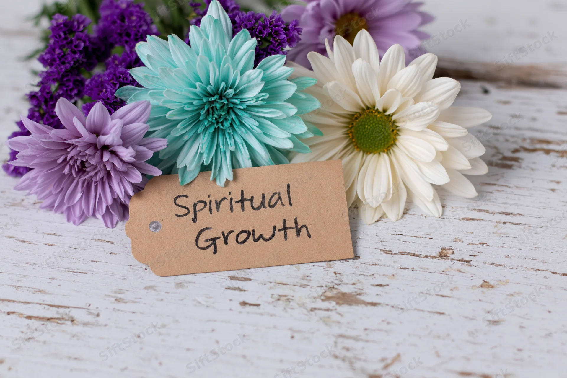 A bouquet of colorful flowers with a kraft paper tag reading spiritual growth on a weathered white wooden surface