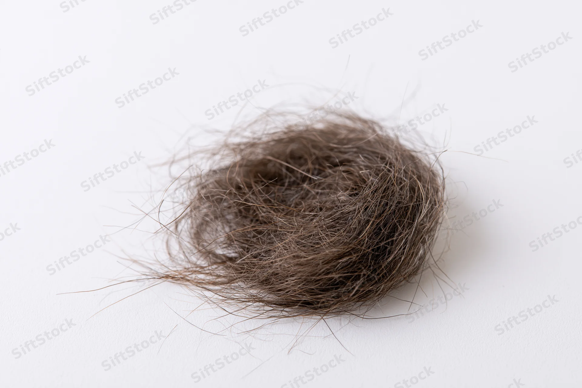 Tangled clump of shed dark brown human hair on white surface