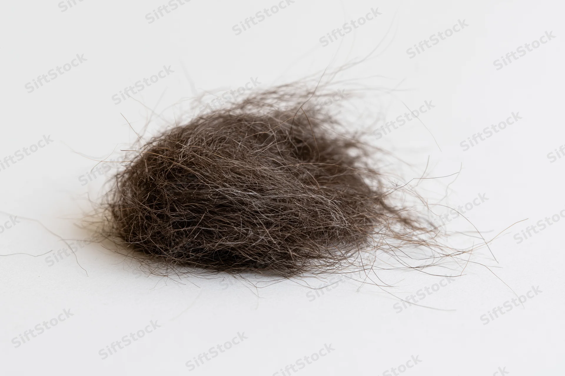 Tangled clump of shed dark brown human hair on white surface