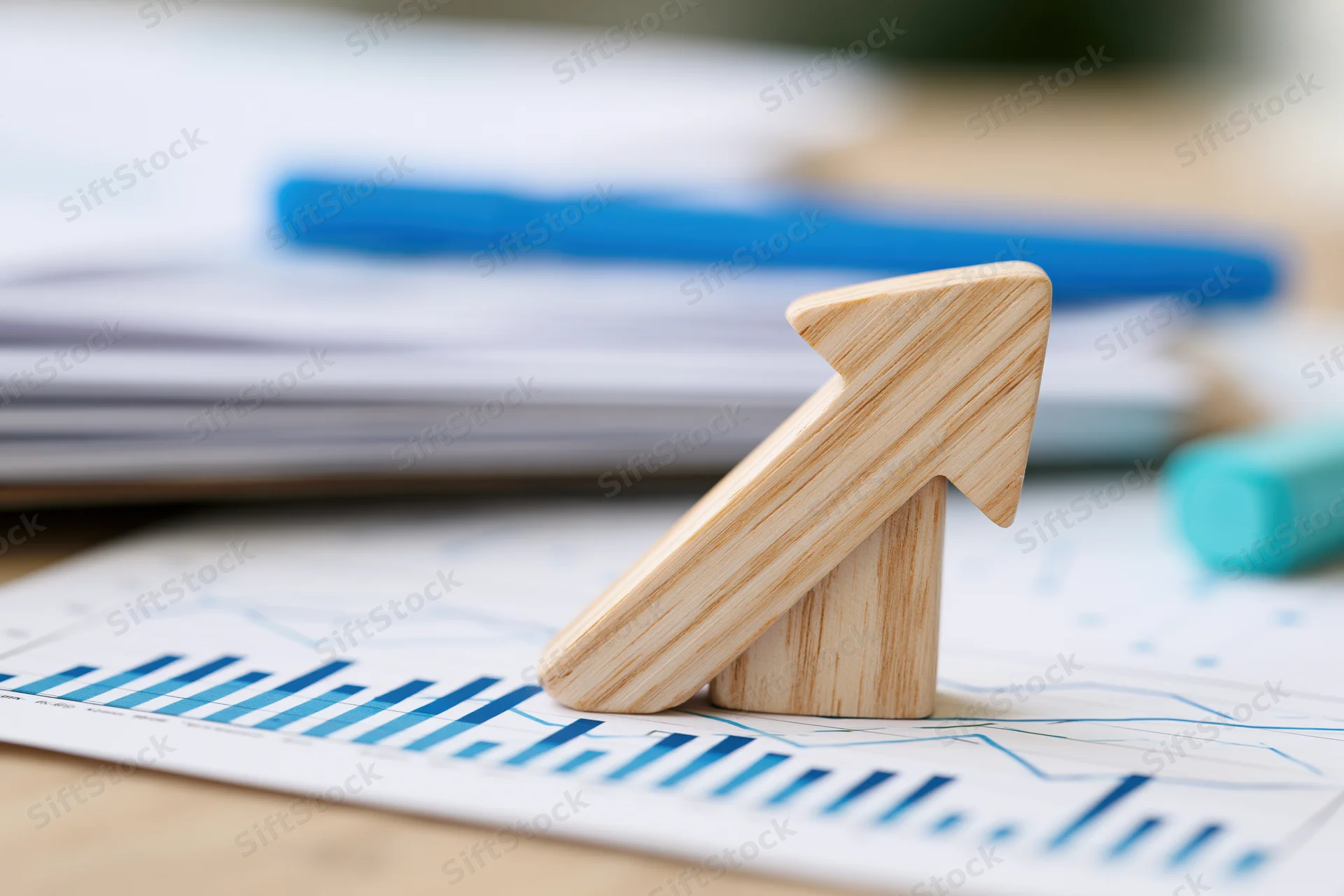 Wooden arrow pointing upward on printed financial chart on office desk