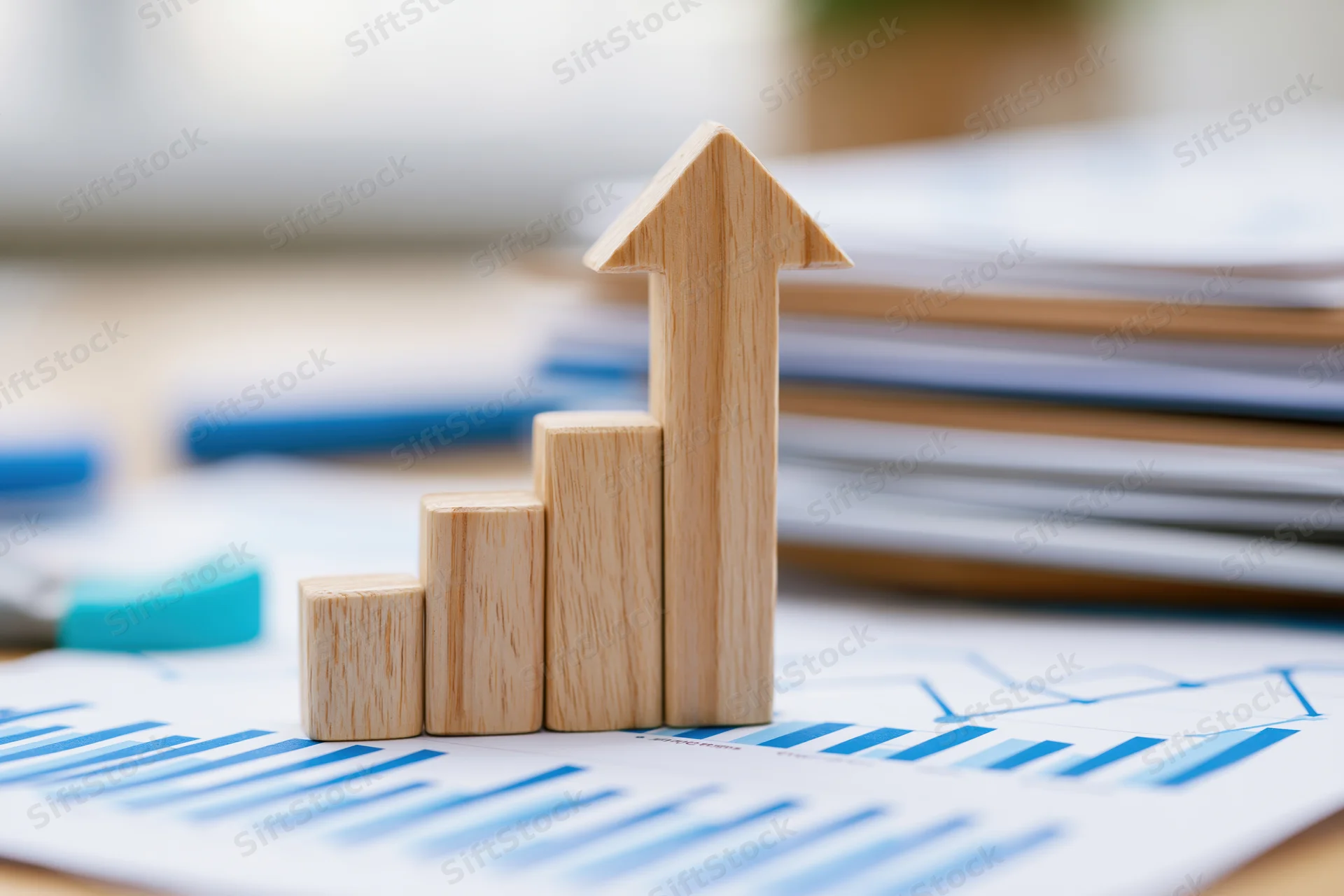 Wooden arrow figurine pointing upward on printed financial charts on office desk