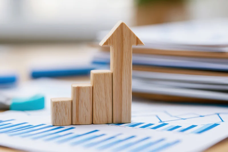 Wooden arrow figurine pointing upward on printed financial charts on office desk