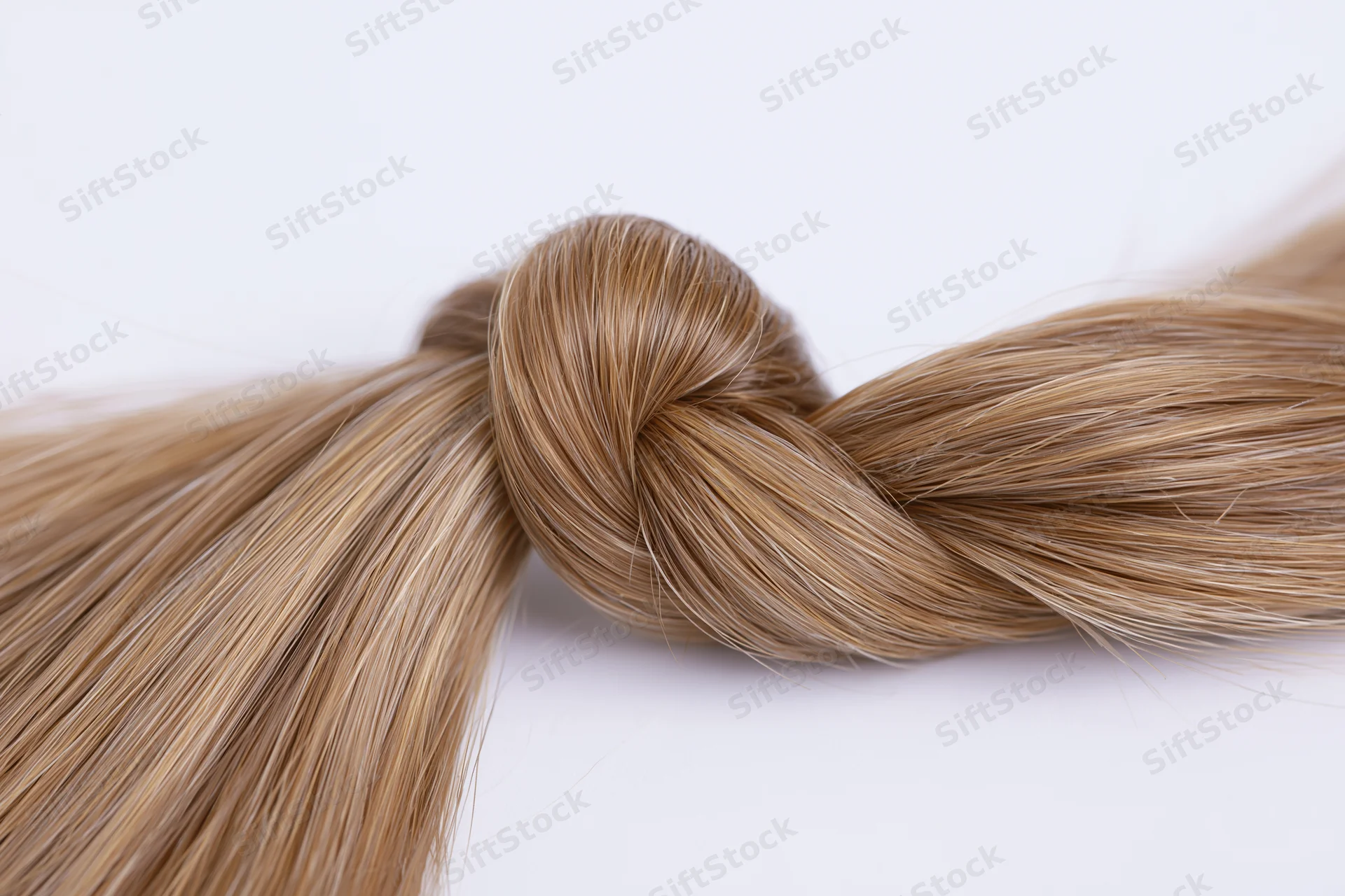 Closeup of a smooth blonde hair strand twisted into a loose knot on white background