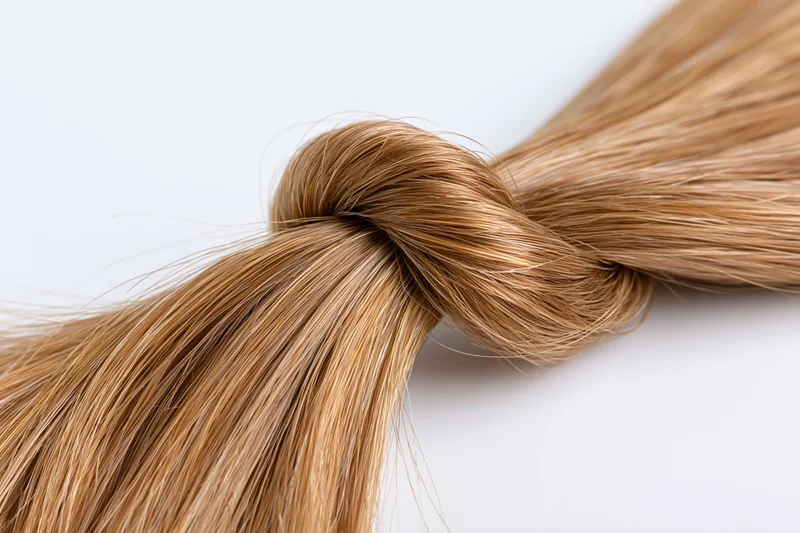 Smooth light brown hair strand twisted into a loose loop on white background