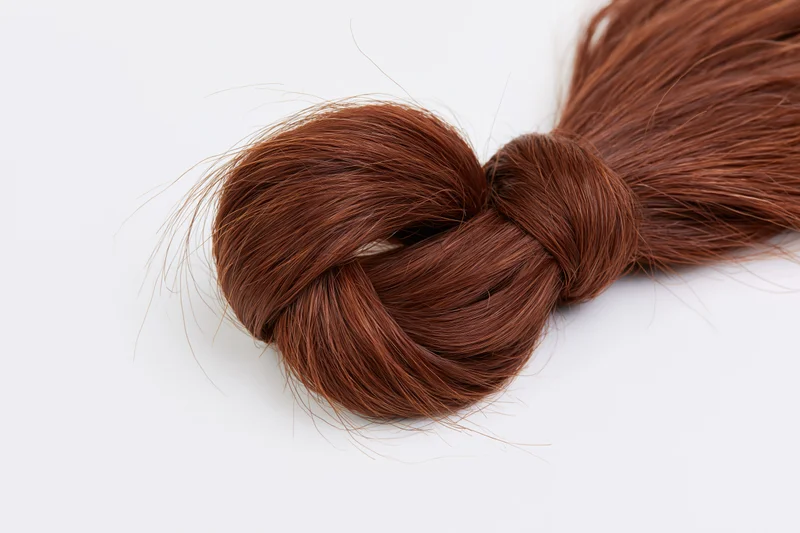 Thick bundle of chestnut brown human hair tied into a loose knot on white background