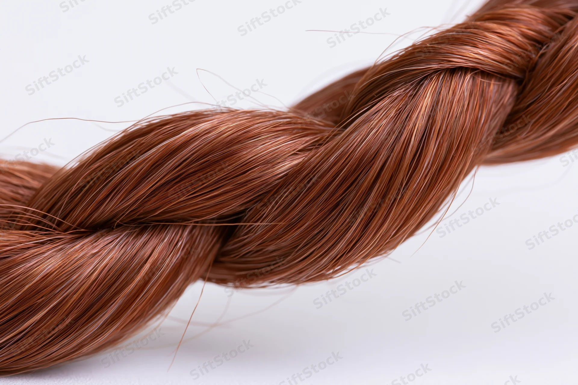Closeup of auburn red hair strand braided into a loose knot on white background