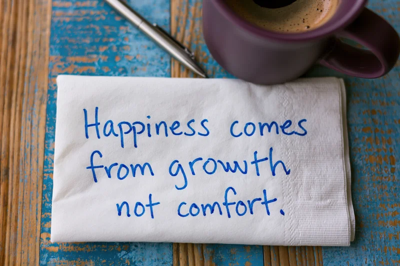 Handwritten motivational quote on a napkin with coffee mug and pen on a wooden table