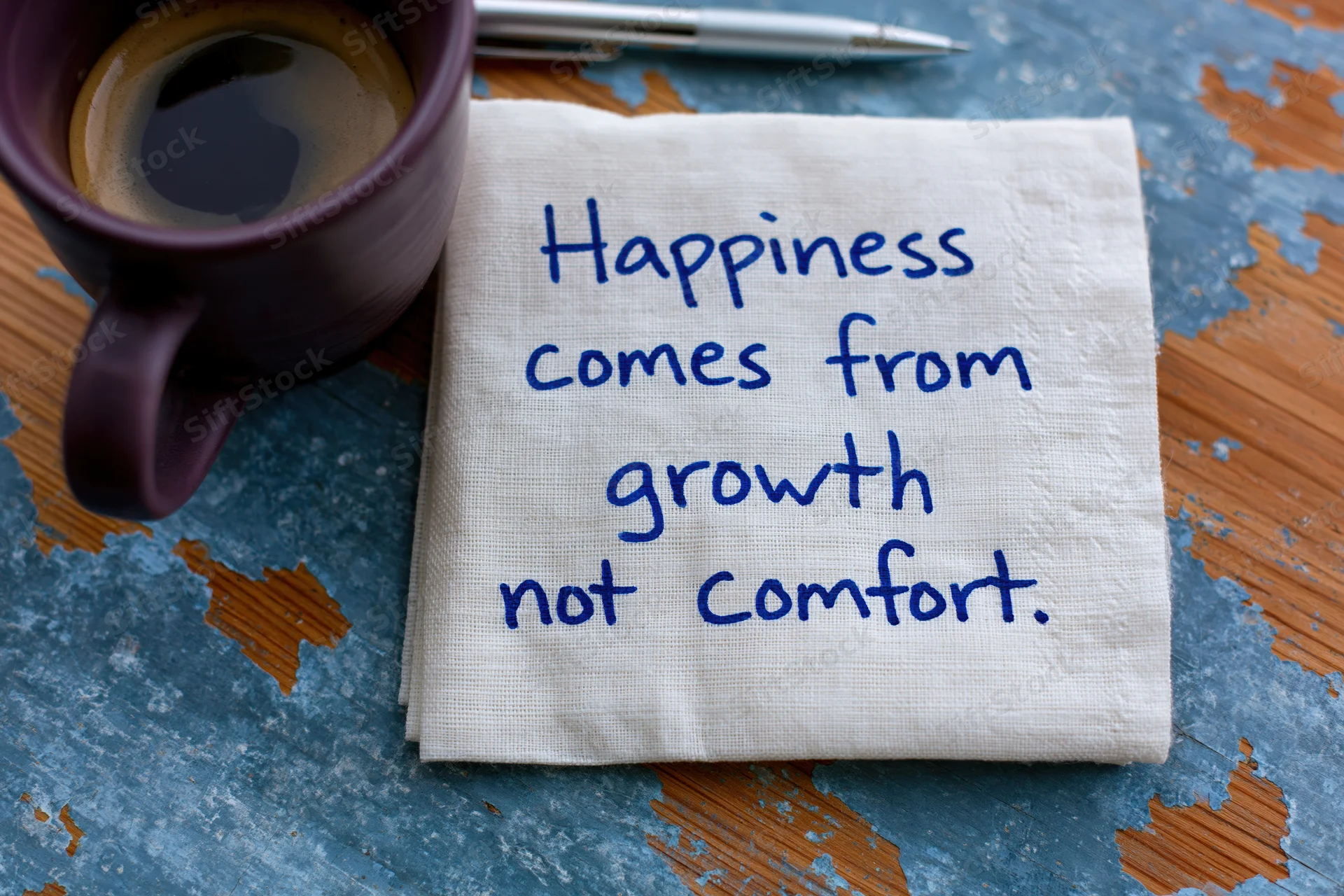 Handwritten motivational quote on a napkin beside a coffee mug on a rustic wooden table